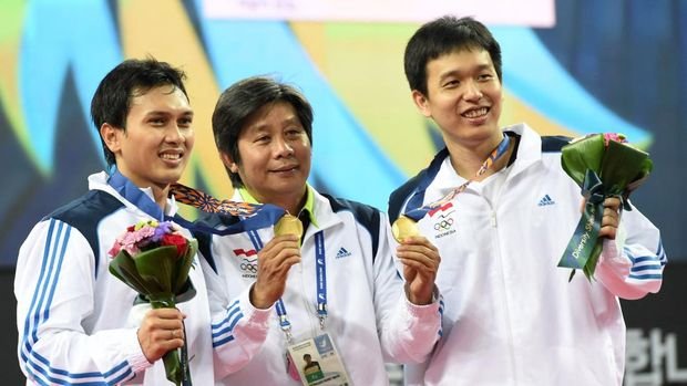 Gold medalists Indonesia's Mohammad Ahsan (L) and Hendra Setiawan (R) pose with their coach Herry Iman Pierngadi (C) on the podium after the men's doubles badminton final at Gyeyang gymnasium during the 2014 Asian Games in Incheon on September 28, 2014.  AFP PHOTO/ROSLAN RAHMAN (Photo by ROSLAN RAHMAN / AFP)