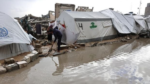 A displaced Palestinians clears water from his tent at a makeshift camp during a storm in Gaza City on December 31, 2024, amid the continuing war between Israel and the militant Hamas group. (Photo by Omar AL-QATTAA / AFP)